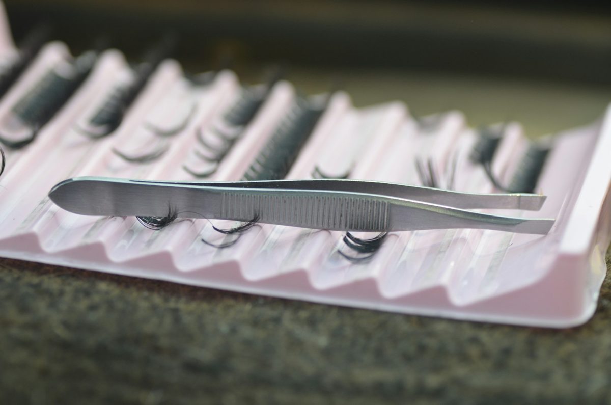 Lash tweezers resting on a tray of lash extensions